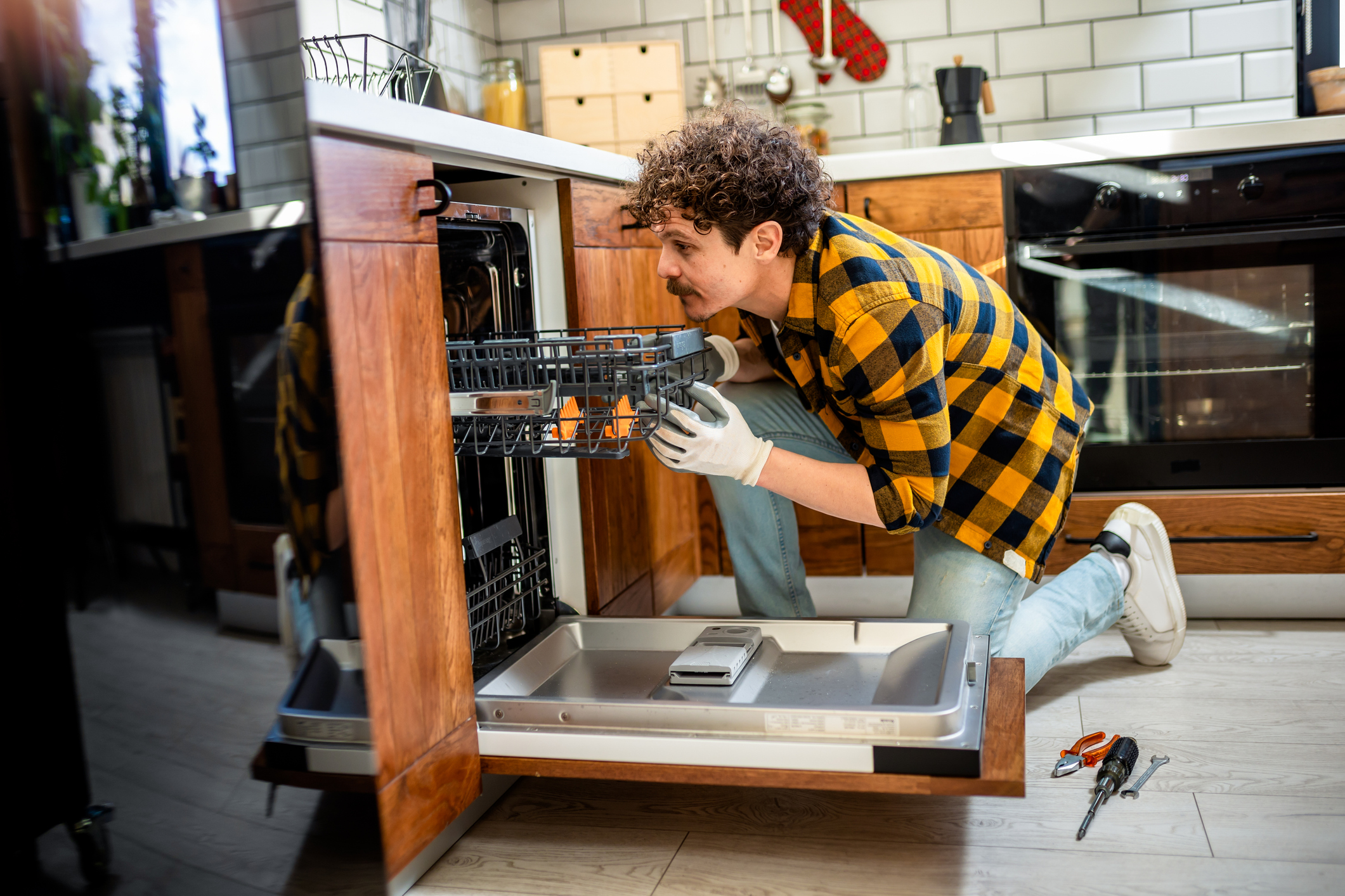 A man in yellow plaid installing a dishwasher at home
